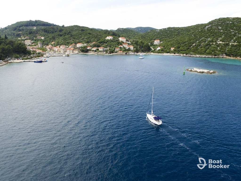 A sailboat’s gliding across a calm bay toward a small coastal village with hills and scattered houses, perfect for sailing in Croatia.