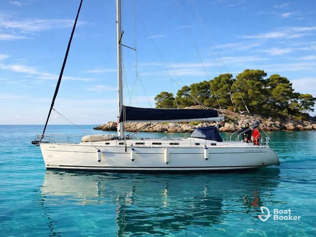 A white sailboat with a dark blue cover floats on clear blue water by a tree-covered island, perfect for sailing in Croatia under a bright sky.