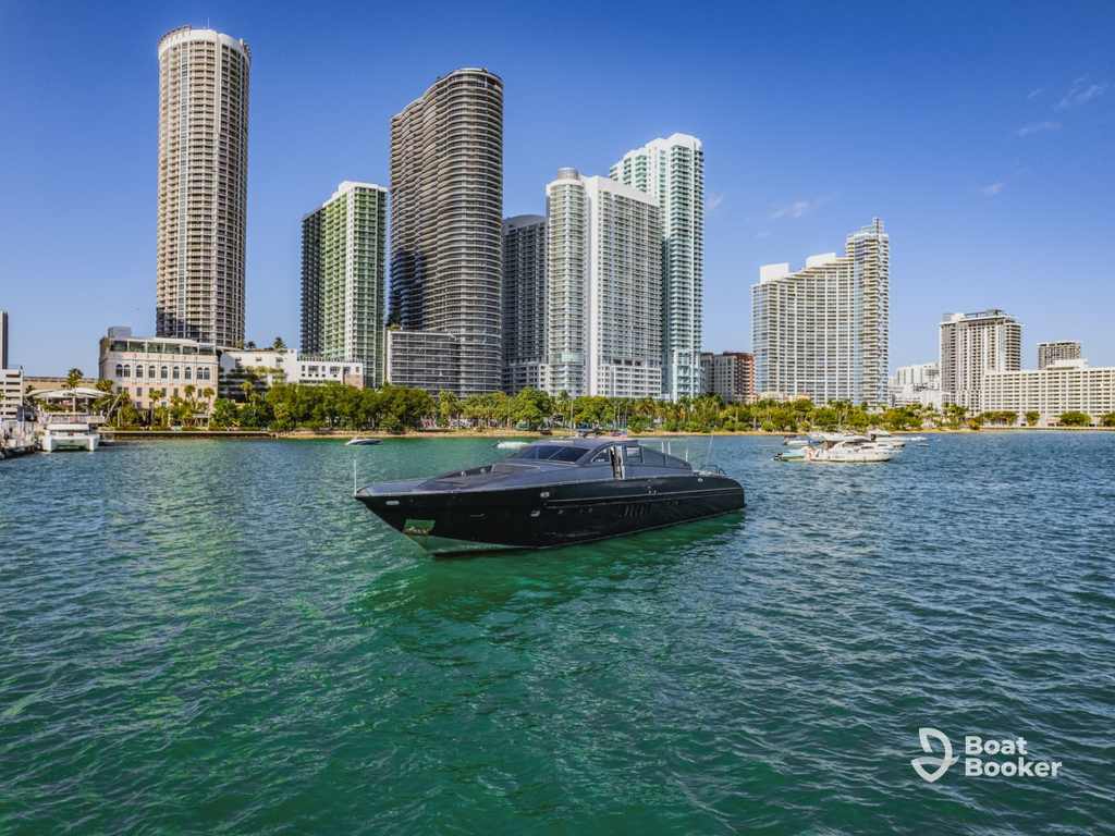 A sleek black yacht—what’s a yacht if not pure luxury—floats on water with tall modern buildings and palm trees in the background under a clear blue sky.