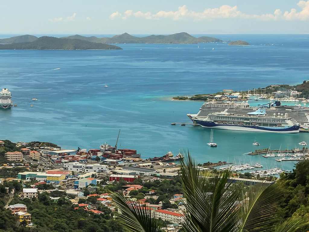 A coastal town’s got colorful buildings, a marina, and two big cruise ships in a turquoise bay, surrounded by small islands.