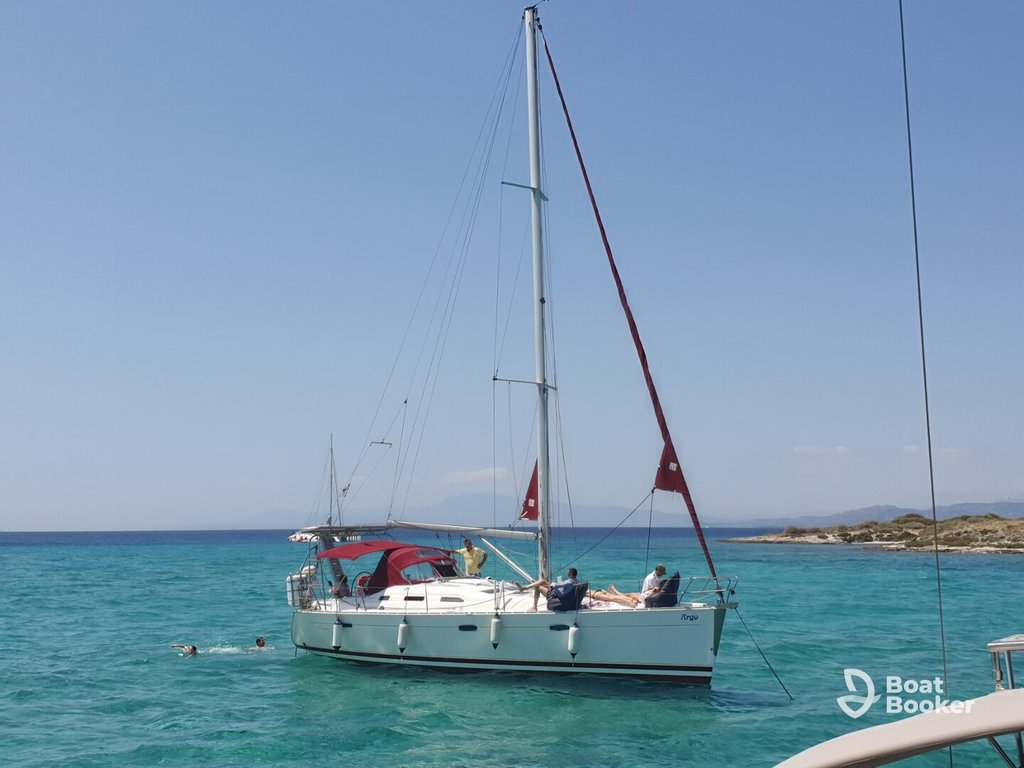 A white sailboat with red details floats on clear turquoise water near a rocky shoreline under a clear blue sky.