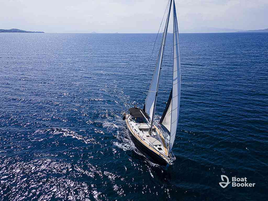 A sailboat with white sails glides across calm, deep blue water under a clear sky. The “Boat Booker” logo’s in the lower right corner.