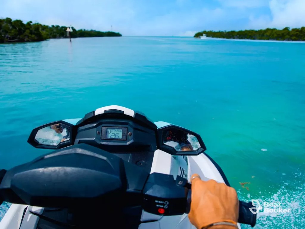 Someone’s driving a jet ski on clear blue water toward green islands under a partly cloudy sky, and you can see the speedometer on the dashboard.