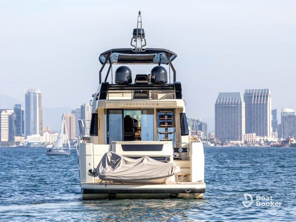 You’re seeing a large yacht from behind on the water, with a city skyline and several buildings in the background.