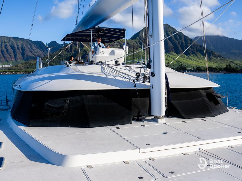 A white catamaran yacht with a shaded flybridge’s anchored on blue water in Hawaii, ideal for island hopping, with green mountains and a blue sky behind.