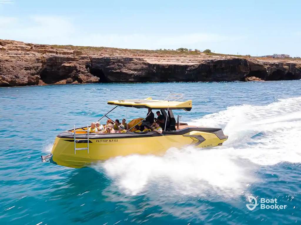 A yellow motorboat with several people onboard’s speeding across blue water near a rocky coastline under a clear sky.