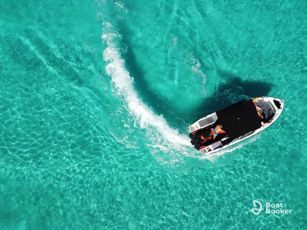 A motorboat with passengers moves through clear turquoise water, leaving a white wake. The Boat Booker logo’s in the lower right corner.