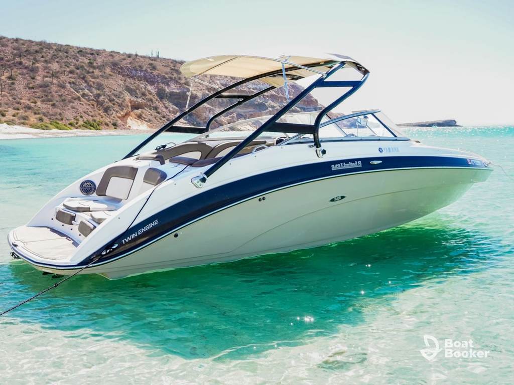 A white and blue speedboat—often mistaken for a Jet Boat—anchors in clear turquoise water by rocky coast under a sunny sky.