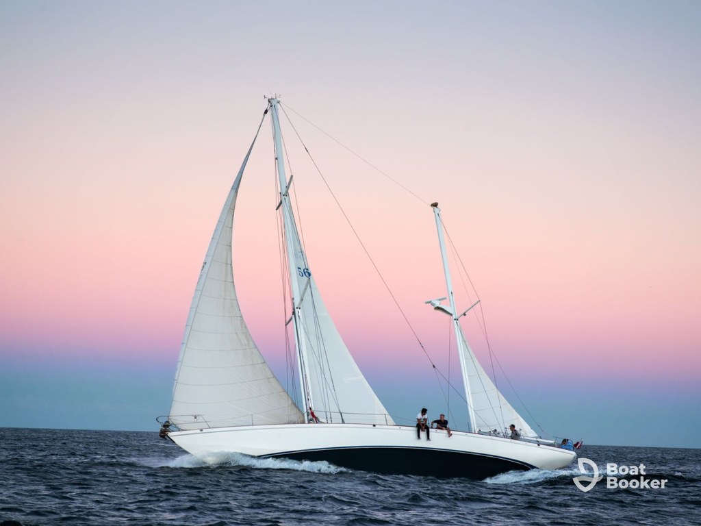 A white sailboat with crew’s cruising the ocean at sunset, pink and blue sky astern. Sailing terms show subtly; “Boat Booker” logo’s in the lower right corner.