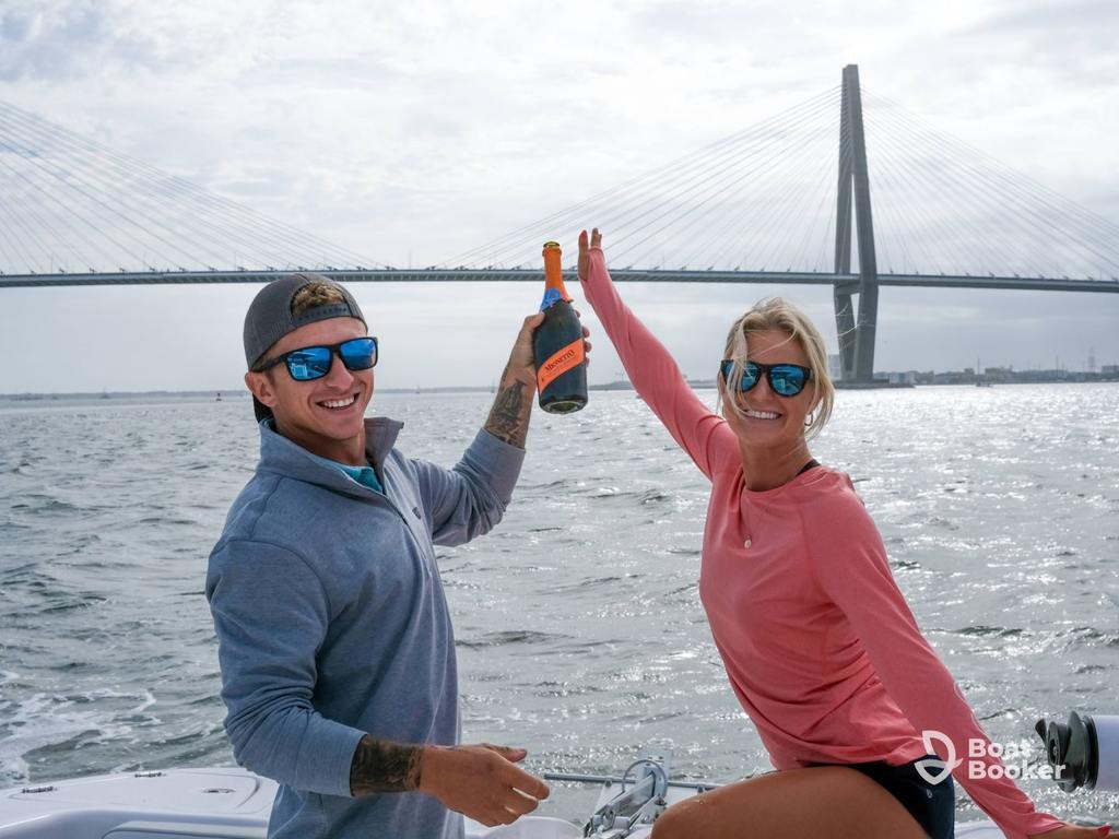 Two people pose with a champagne bottle on a boat under a cable-stayed bridge—don’t forget your South Carolina boating license for fun days like this!