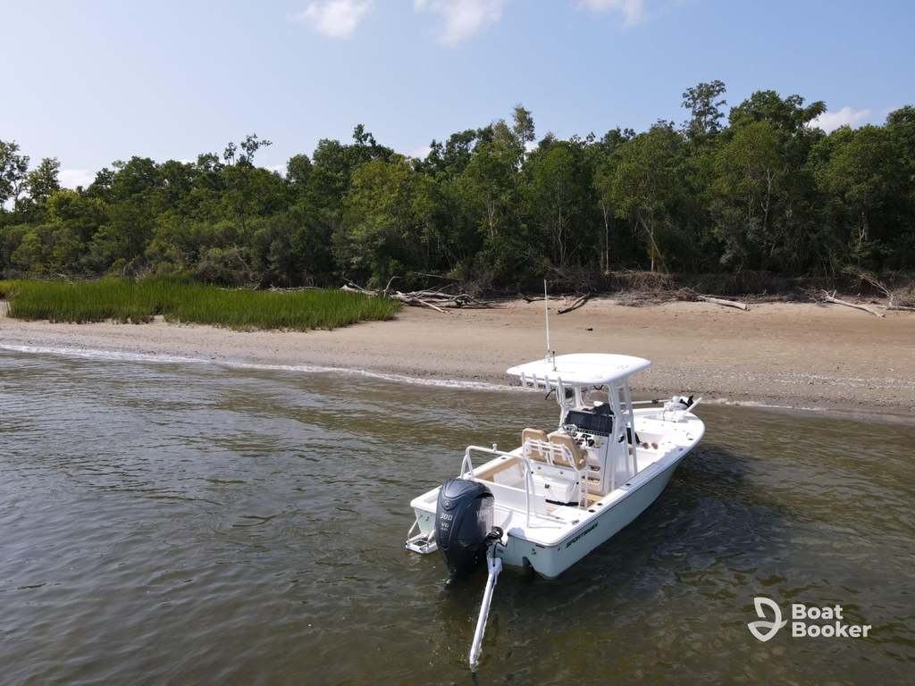 White motorboat’s anchored in shallow water by a sandy beach and dense green trees. It’s the perfect spot to enjoy with your South Carolina boating license. Boat Booker logo’s at bottom right.