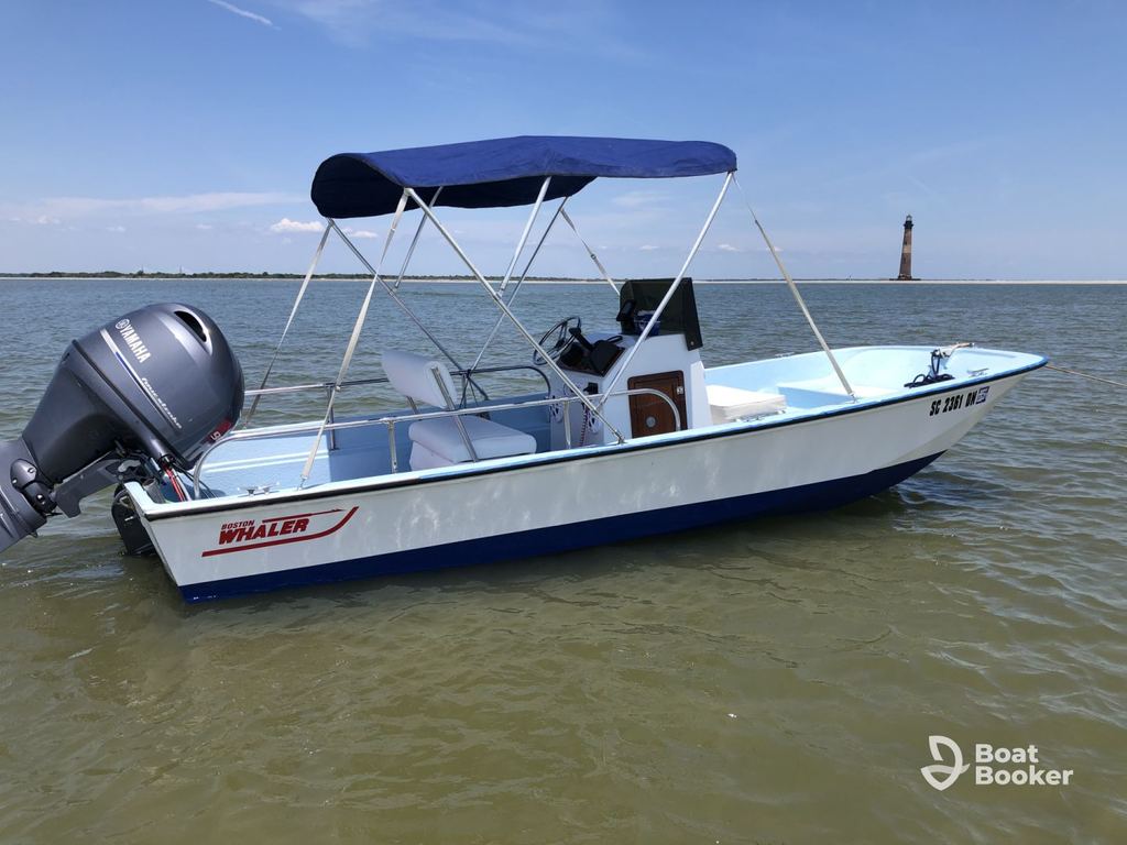 A small motorboat with a canopy floats quietly—reminding everyone you’ll need a South Carolina boating license to enjoy these peaceful waters near the distant lighthouse.