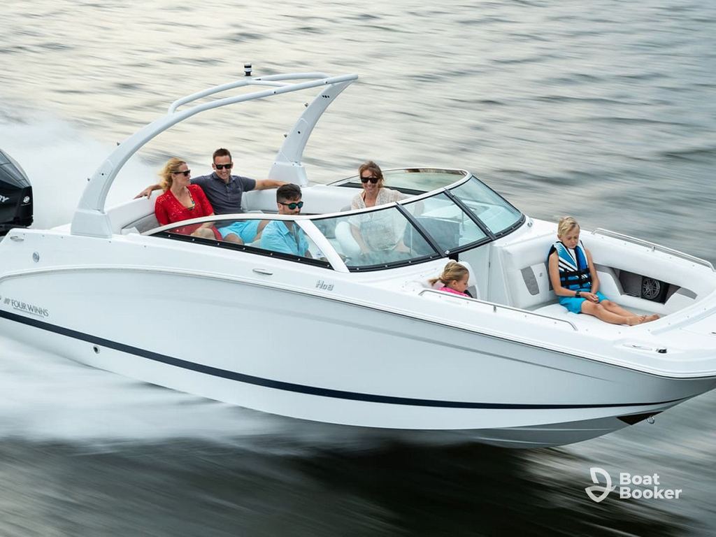 A white runabout boat with six people, including kids and adults, speeds across the water, making waves behind it.