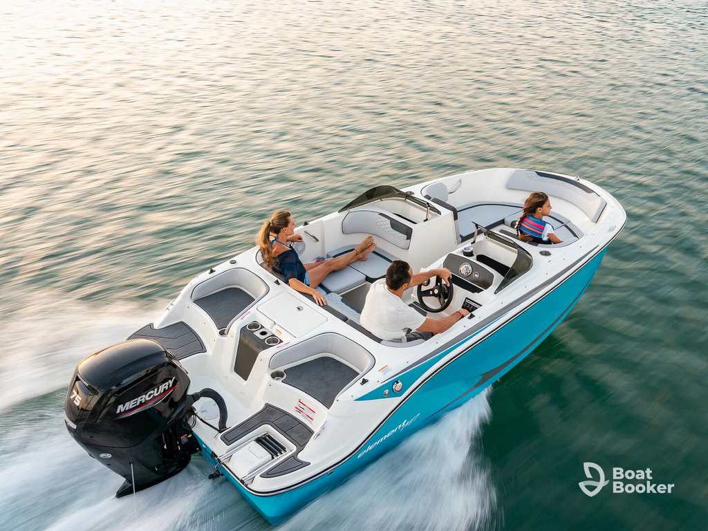 Three people’re riding a small blue and white runabout boat over calm water. One’s steering while two relax, and the boat leaves a gentle wake behind it.