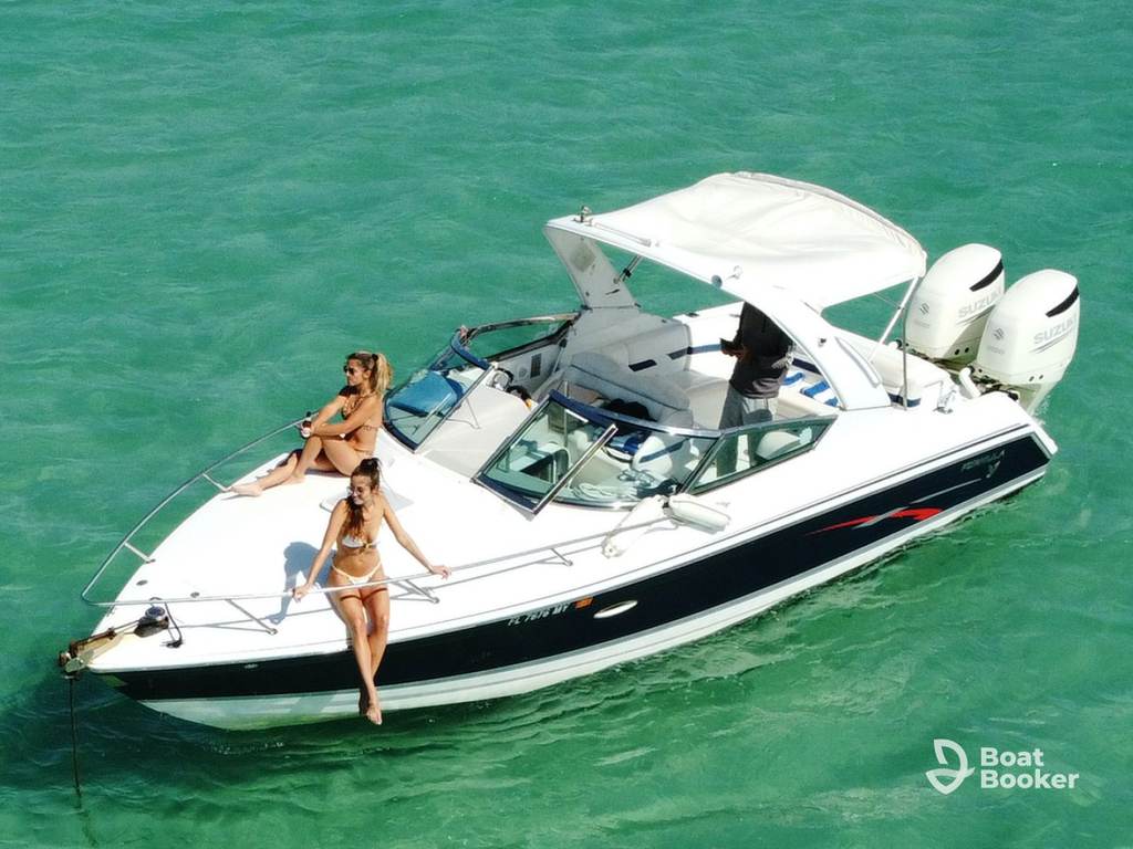 A motorboat, often called a runabout, with two women in swimsuits at the bow and one person steering, floats on clear turquoise water.
