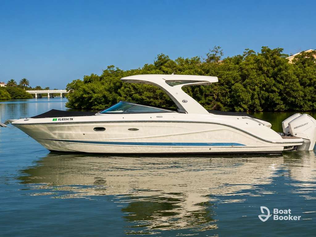 A white runabout motorboat with a hardtop canopy floats near lush mangroves; a bridge and blue sky frame the scene. The Boat Booker logo’s in the bottom right corner.