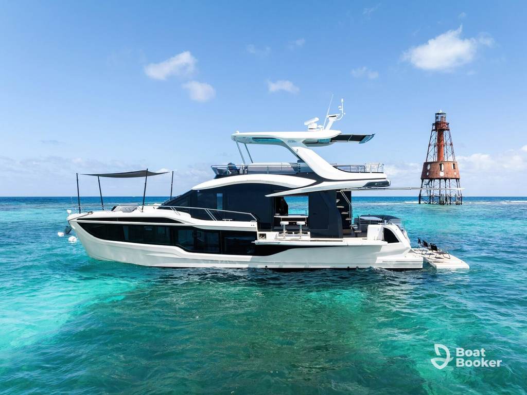 A white luxury yacht, run by a captain with a New York boating license, is anchored in clear turquoise water near a rusty lighthouse under a blue sky.
