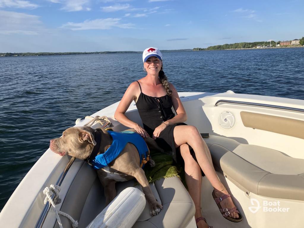 A woman and her brown dog in a blue life jacket relax on a calm lake, both ready for adventure after she’s earned her New York boating license.