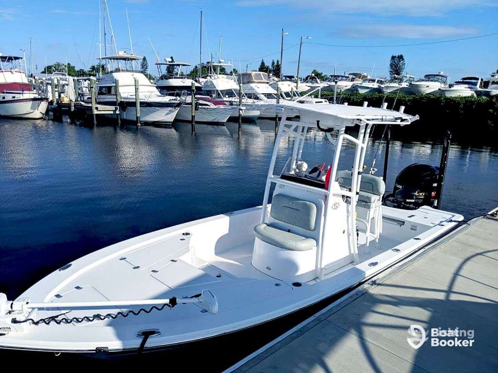 A white motorboat’s docked at a marina, with several other boats in the background under a clear blue sky.