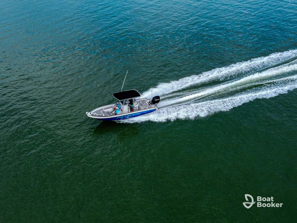 A small motorboat speeds across open water, leaving a white wake behind. Two people are onboard. The Boat Booker logo’s in the bottom right corner.