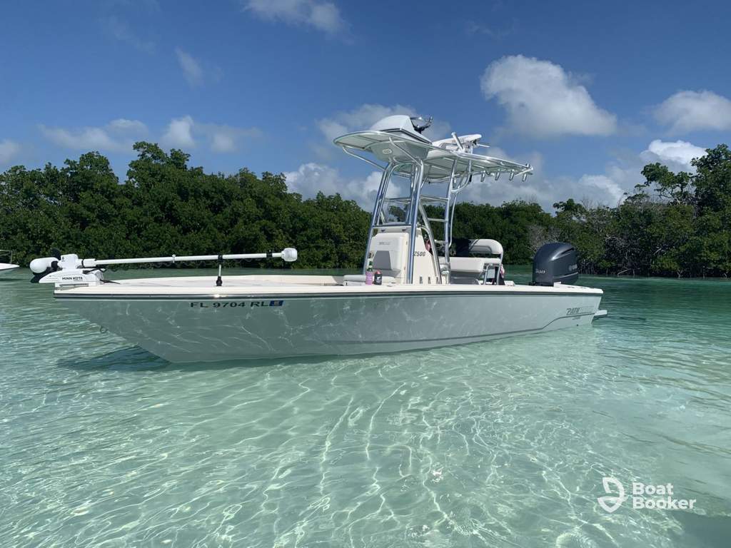 A white center console boat’s anchored in clear, shallow water near a mangrove shoreline under a partly cloudy sky.