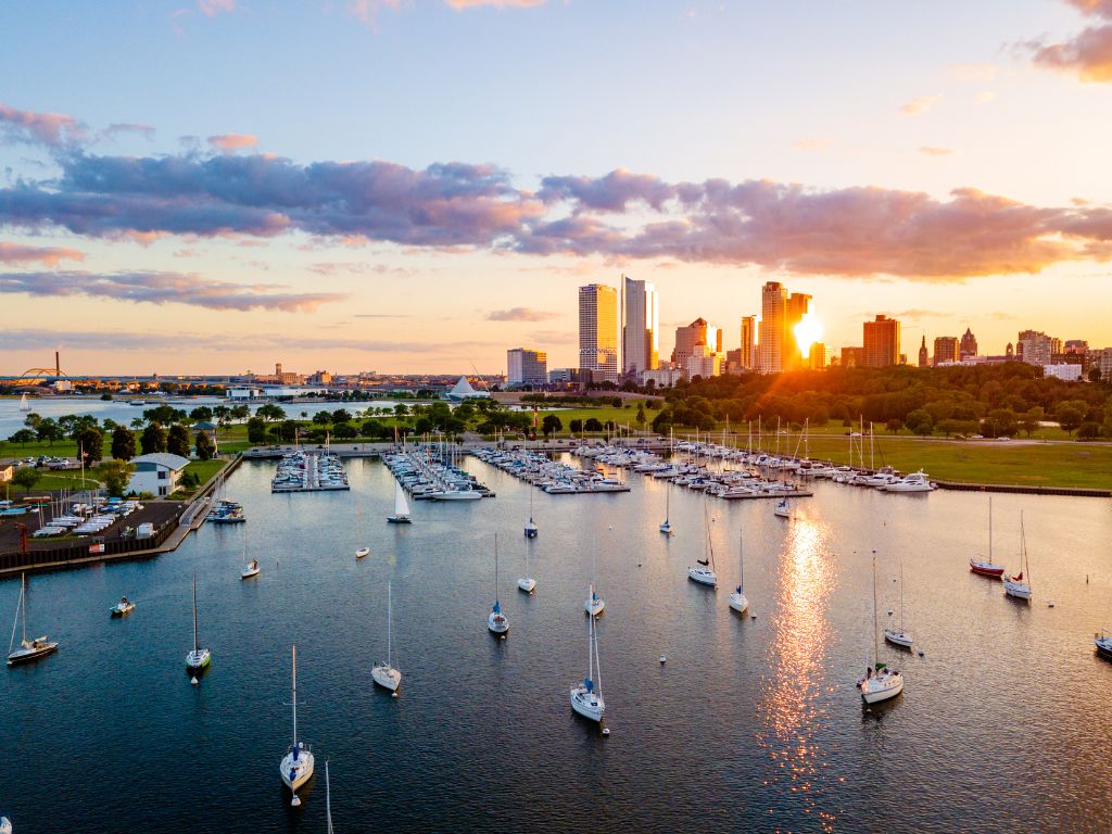 A marina with many docked boats sits up front, showing one of the top boating states. There’s a city skyline and sunset in back under partly cloudy skies.