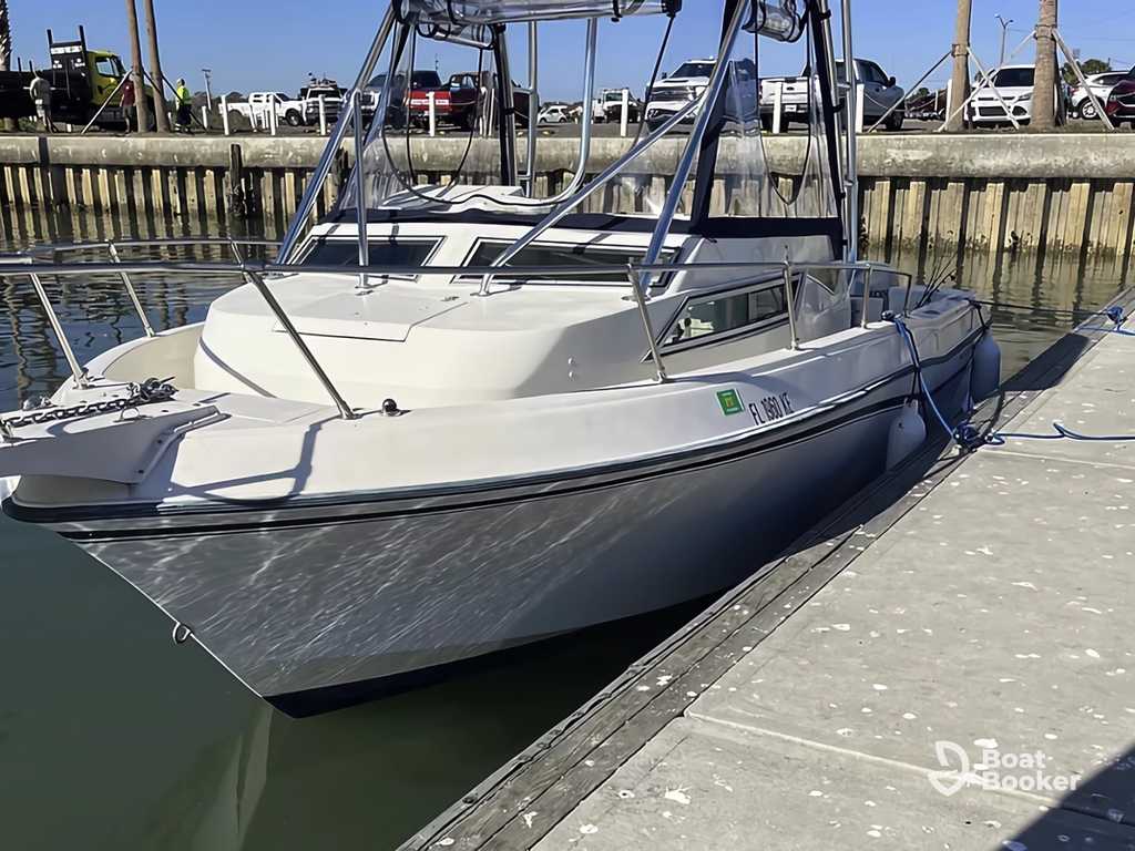 White and gray motorboat docked at a marina with a concrete pier, wooden railing, and parked cars—it’s perfect for folks curious what a cuddy cabin’s used for on small boats.