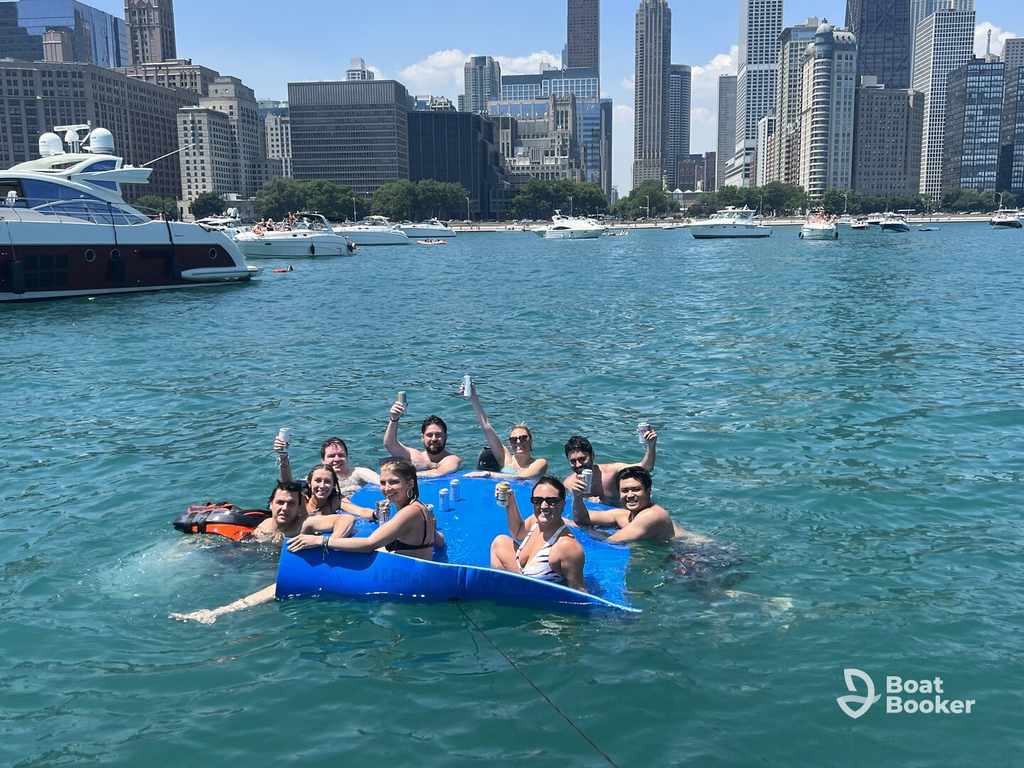 Ten friends float on a blue mat in a city harbor, drinks in hand, enjoying sunny skies and boats—it’s the perfect day for anyone with an Illinois boating license.